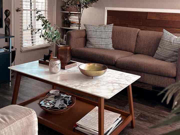 Brown and wood-tone living room featuring a brown sofa and white marble coffee table with tray and metal bowl, creating a natural atmosphere