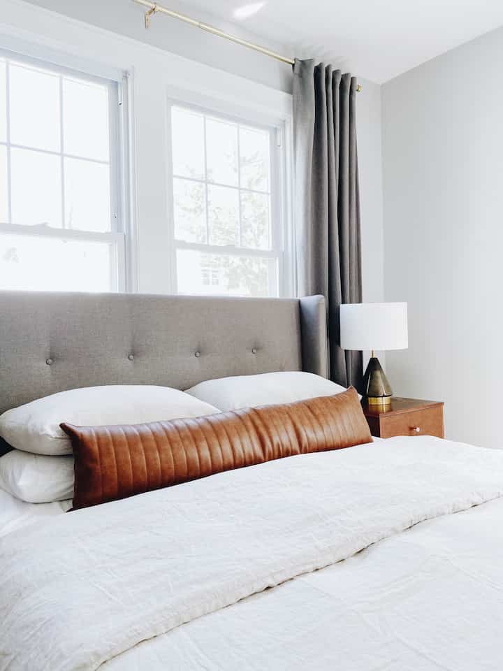Modern bedroom with bright white walls, gray upholstered bed headboard, and dark gray blackout curtains creating a calm atmosphere