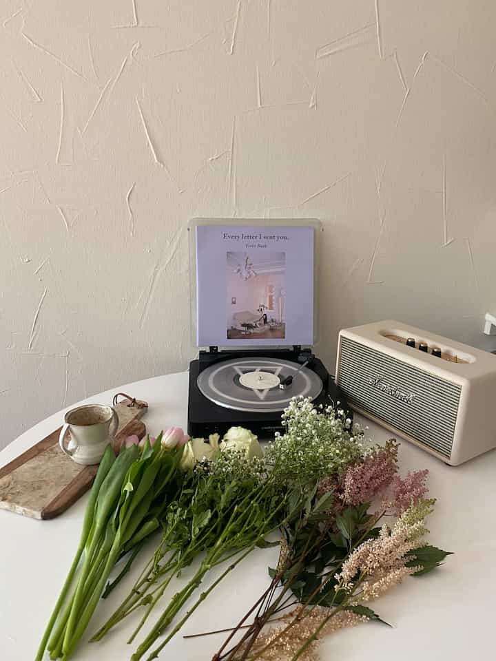 White and beige toned living space featuring fresh flowers on table, record player and Marshall speaker, creating a cozy atmosphere