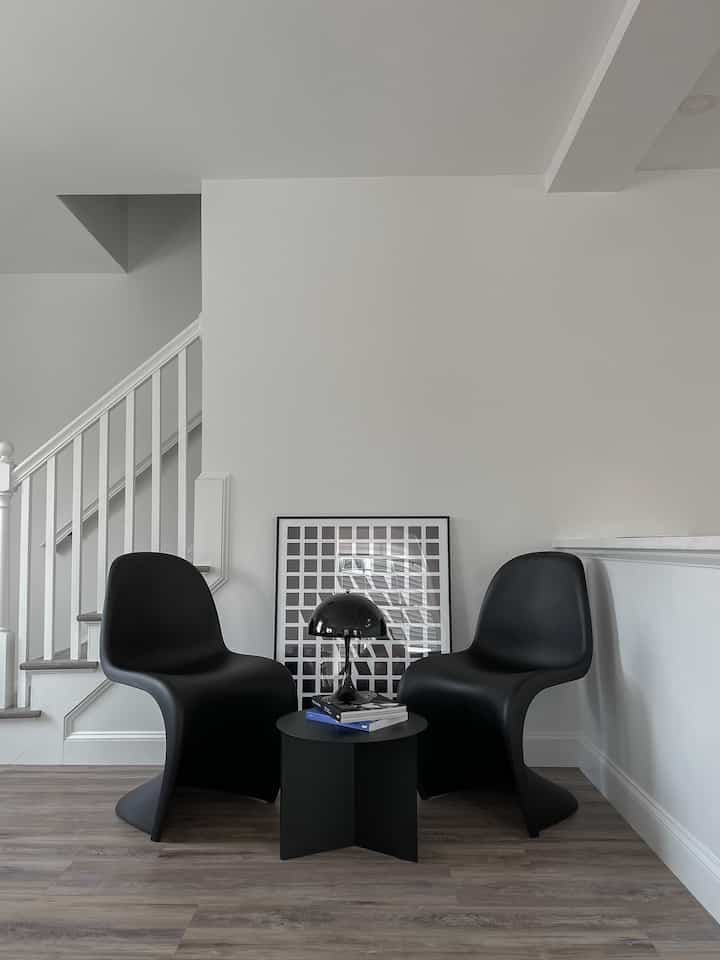 Modern corner space with white walls, natural wood floor, and black Panton chairs with table lamp
