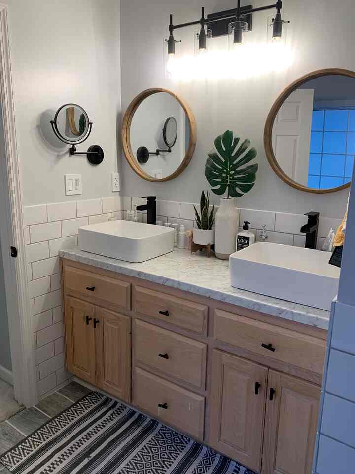 Earthy wood tones and black accents featuring farmhouse style bathroom with round wooden mirrors and matte black faucets