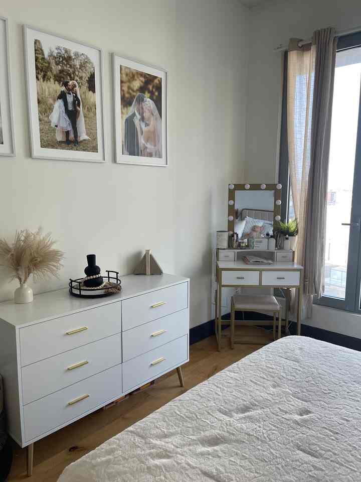 White bedroom with gold accents featuring dresser and vanity, bright natural light creating a clean and natural atmosphere