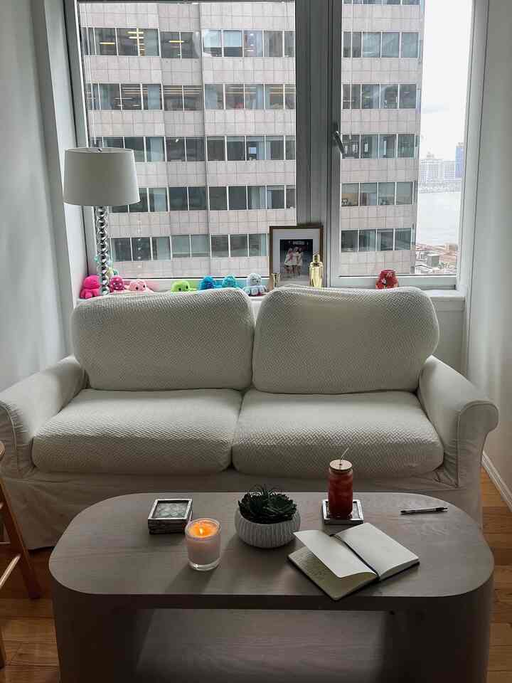 Narrow living room with white sofa and wood tone coffee table, natural light entering through large windows creating a cozy atmosphere