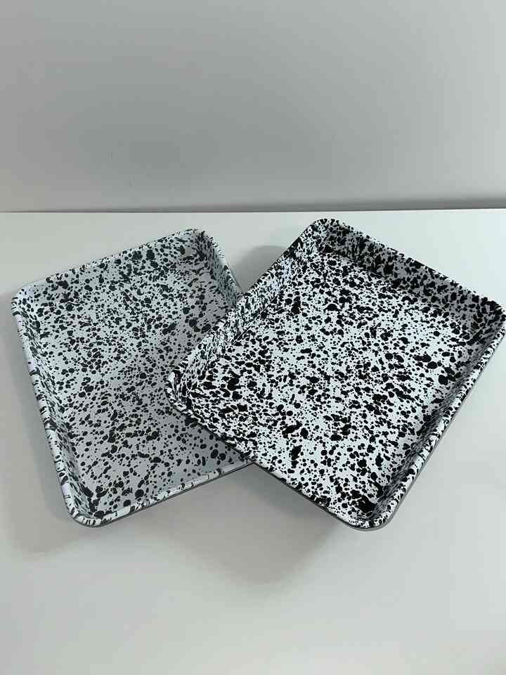 Simple and clean kitchenware image featuring two rectangular trays with black splatter patterns on a white table