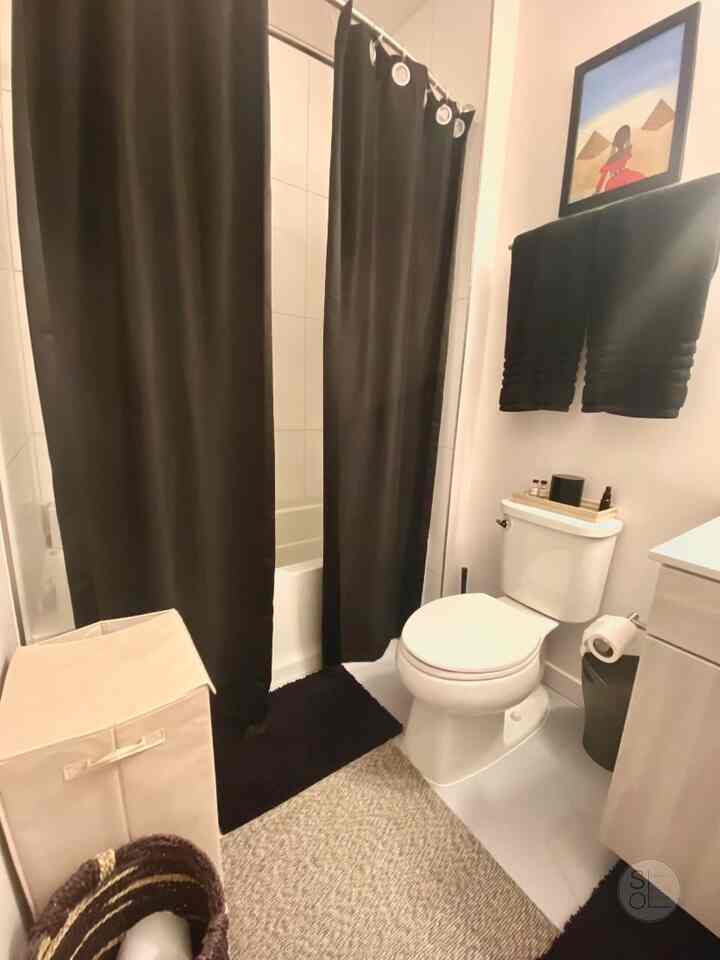 Cozy bathroom space featuring black blackout curtains and bath mat with clean, minimalistic design