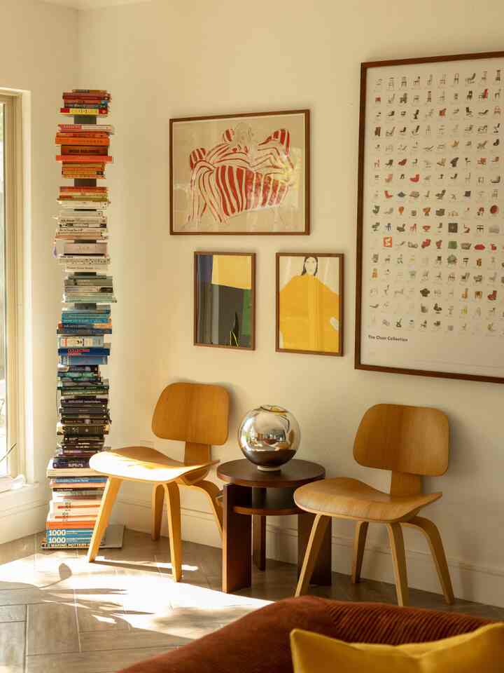 Natural tone living room corner featuring two wooden chairs, a side table, and colorful posters with a warm atmosphere