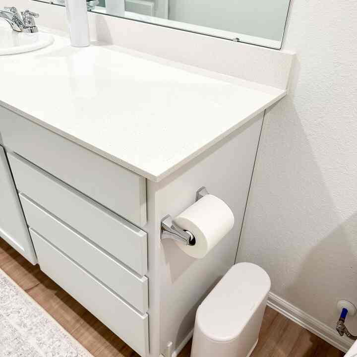 White-toned bathroom featuring modern vanity, automatic soap dispenser, and slim trash can arranged in a clean layout