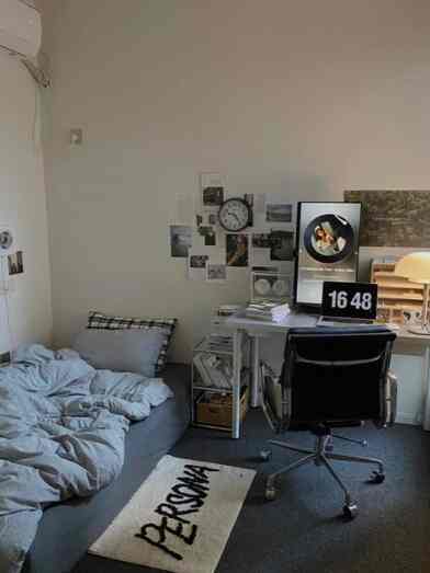 A compact gray and black-toned room featuring a sofa bed, office chair, and desk setup creating a functional home office