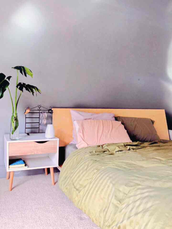 Cozy bedroom with gray wall, natural wood bed frame, nightstand, and green plant arrangement