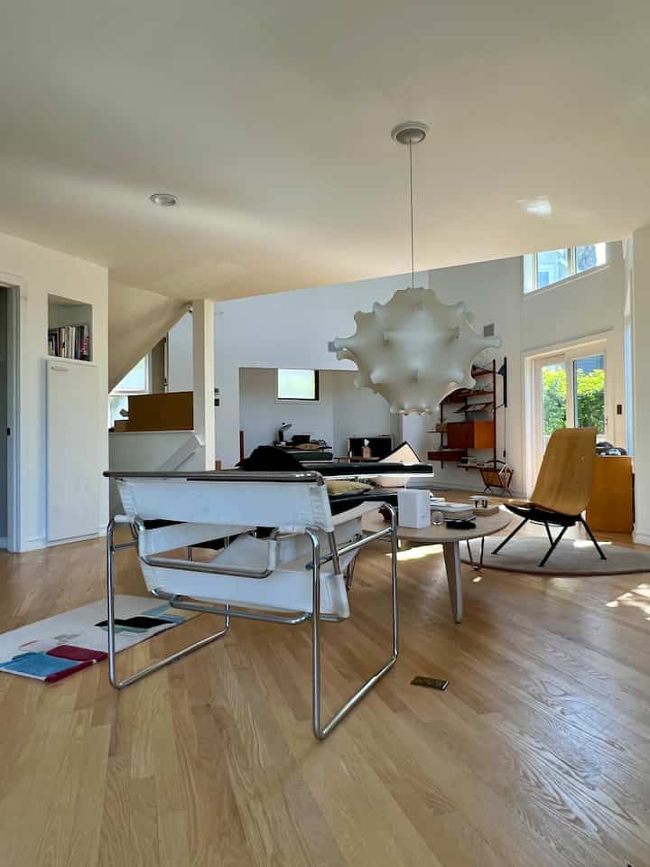 Mid-century modern living room with white and wood tones, featuring Noguchi coffee table and Wassily chair arranged centrally in a cozy space
