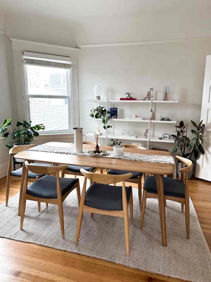 A bright dining room featuring white walls, wood-toned furniture, and natural decor with plants creating a clean and cozy atmosphere