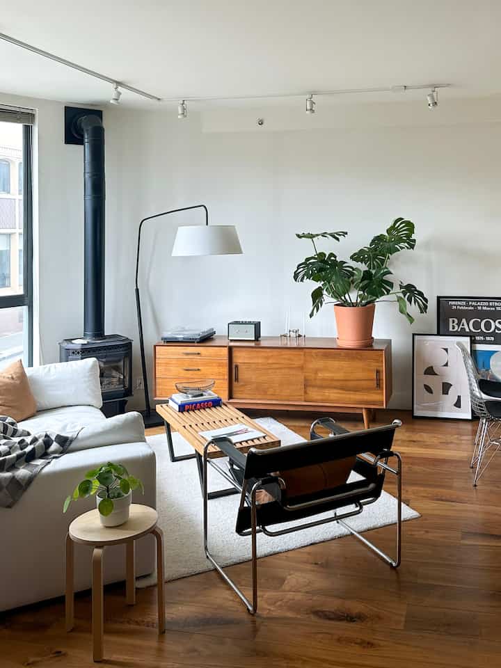 Bright white and brown wood-toned mid-century modern living room featuring a large sofa, mid-century media console, and green plants