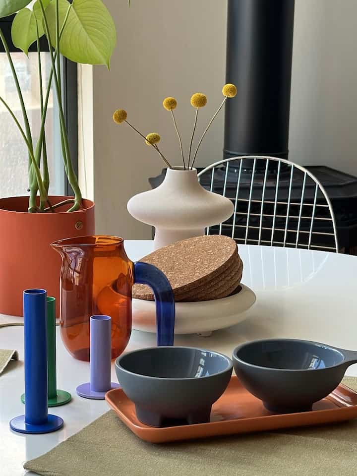 White and natural toned dining room featuring a round table with placemat, pitcher, cork coasters neatly arranged in a simple setting