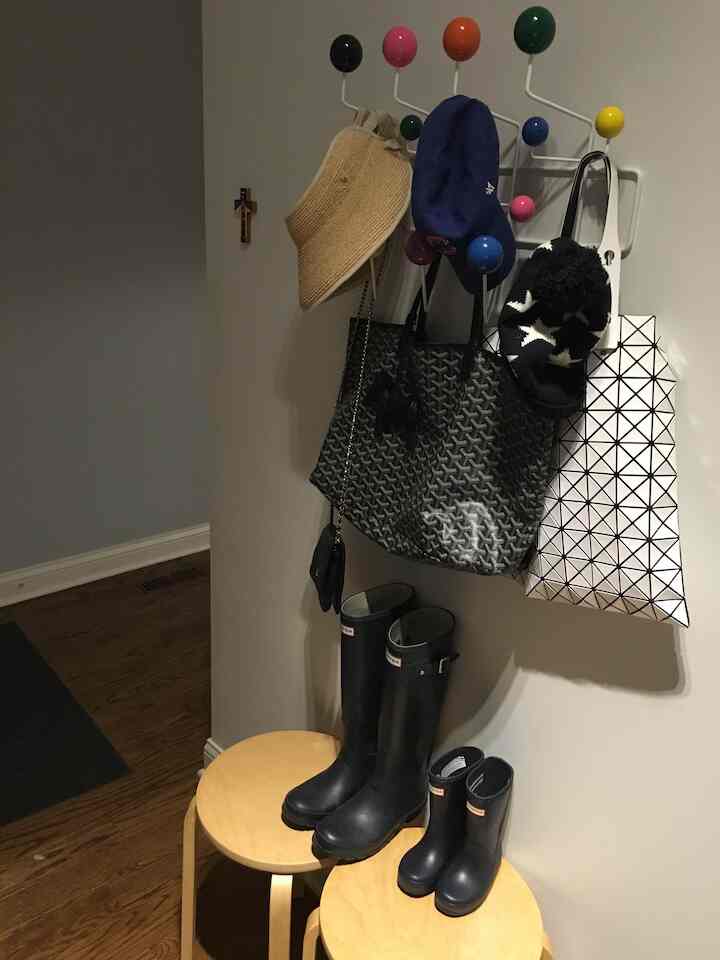 Black and wood tone entrance space featuring colorful coat rack and boots on stools in a neat compact setting