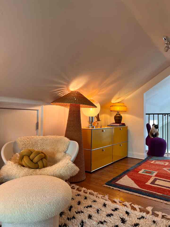 Cozy loft space with warm wood flooring, yellow sideboard, rattan floor lamp, and a cat on a purple chair