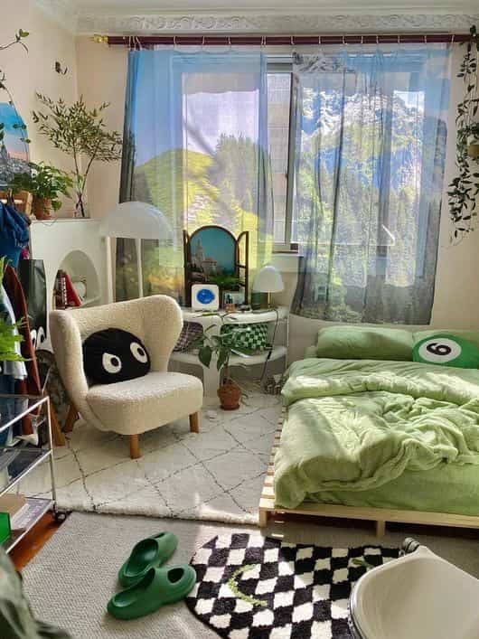 Natural tone bedroom featuring green bedding, cream armchair, large window, and plants creating a cozy atmosphere