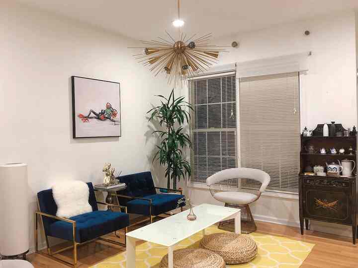Modern living room with white walls, gold lighting fixture, and blue armchairs