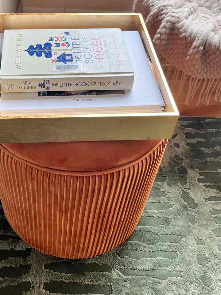 Cozy reading spot with orange pleated ottoman topped by gold tray and books