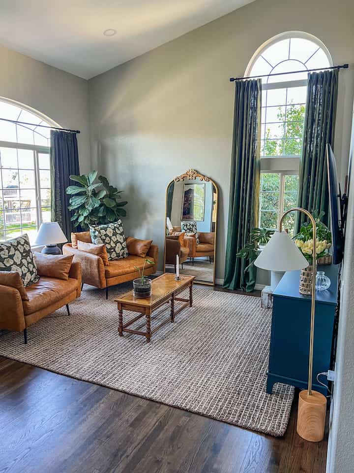 Natural brown and green toned living room featuring leather armchairs, curtains, and a large ornate mirror in a modern setting