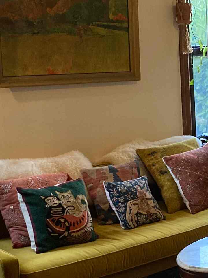 Beige-walled living room with mustard sofa featuring patterned pillows, creating a warm and vintage atmosphere