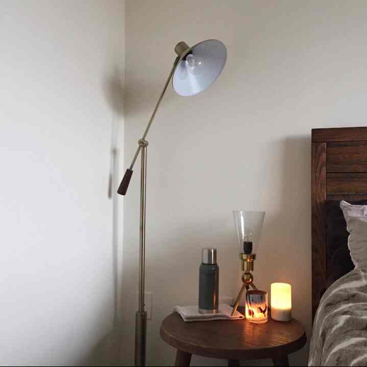 Warm brown wood-toned bedroom with a wooden side table, gold floor lamp, and aroma diffuser creating a cozy atmosphere