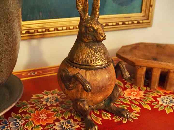 Warm wood tones and gold bronze objects on tabletop featuring a rabbit-shaped box, vase with peonies, and a cat in a cozy interior space