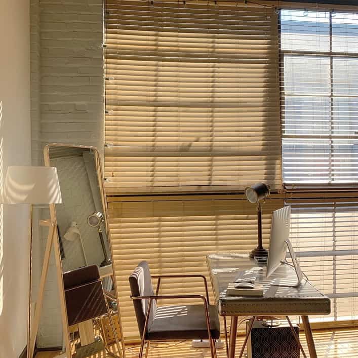 Beige blinds, full-length mirror, desk, and floor lamp arranged in a sunlit home office space