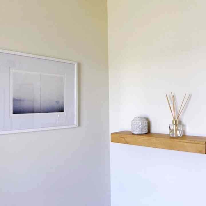 Simple bathroom space with warm white walls and wood tone floating shelf, minimal accessories