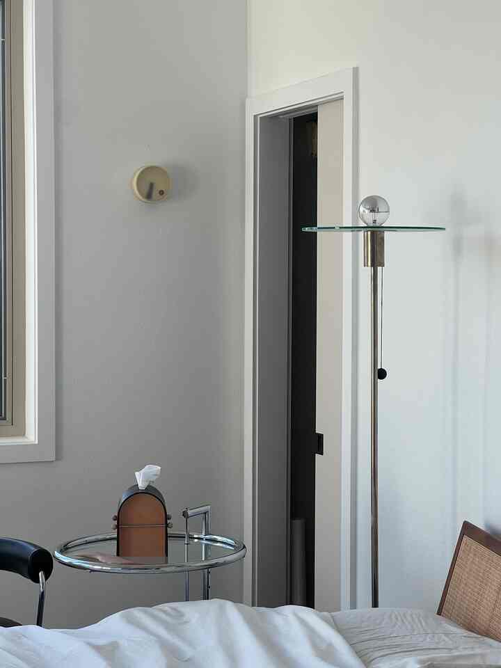 A modern and minimal bedroom with dominant white and natural wood tones featuring a bed, nightstand, and floor lamp