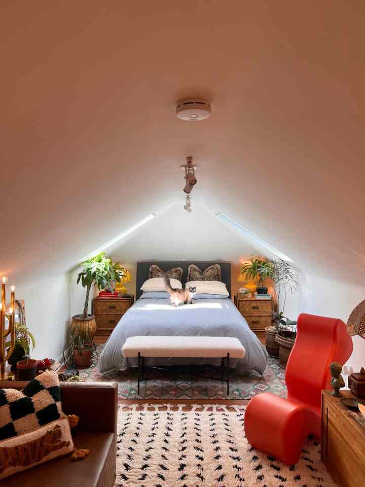 White slanted ceiling loft bedroom with wooden furniture and multiple plants creating a cozy atmosphere