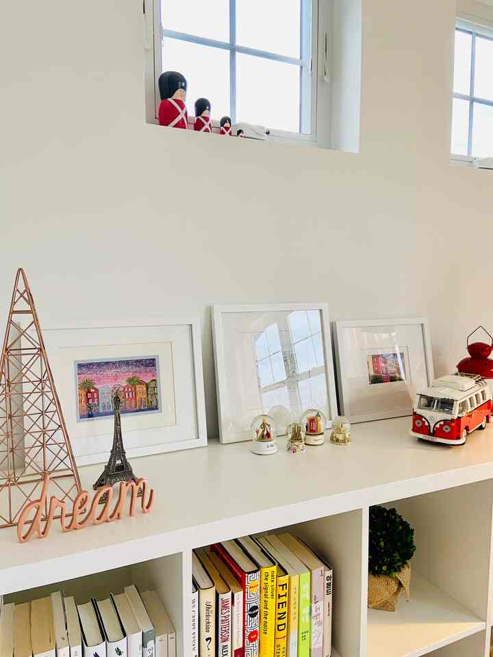 White-toned room featuring a white bookshelf with books below and various picture frames and objets arranged neatly on top