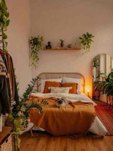 Beige-toned bedroom with wood-tone flooring, cozy orange blanket and lush plants as accent elements
