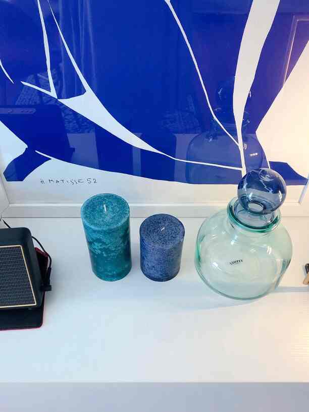 Blue-toned background featuring transparent glass bottle and two decorative candles on a white tabletop