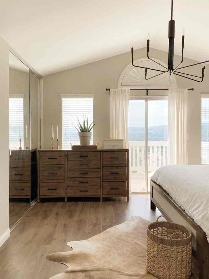 Bright natural modern bedroom in white and wood tones featuring a large dresser and white curtains with a clean, airy atmosphere