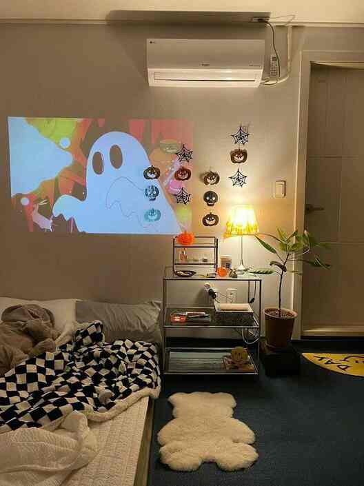Black and white toned small room featuring cozy blankets and a bear-shaped rug with a projector displaying Halloween images for a home cinema atmosphere