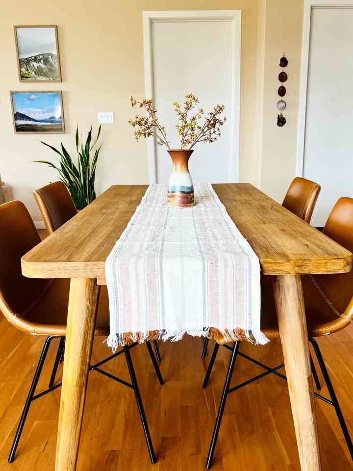 Natural brown toned dining room featuring wooden dining table, leather chairs, white striped table runner, and decorative vase for a clean look