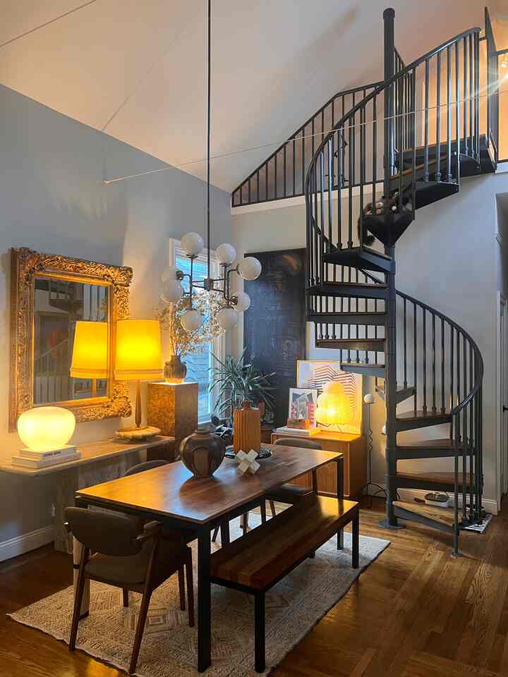 Natural modern wood-tone dining room featuring a black spiral staircase with warm ambient lighting creating a cozy atmosphere