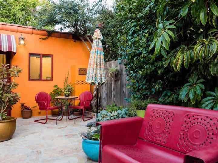 Vibrant orange wall and red outdoor furniture with plants in a bohemian style balcony setting