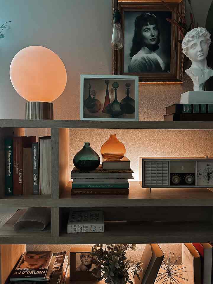 Wood tone brown bookshelf dominates a mid-century modern styled home gallery space with gold lighting and vintage decor creating a cozy ambiance