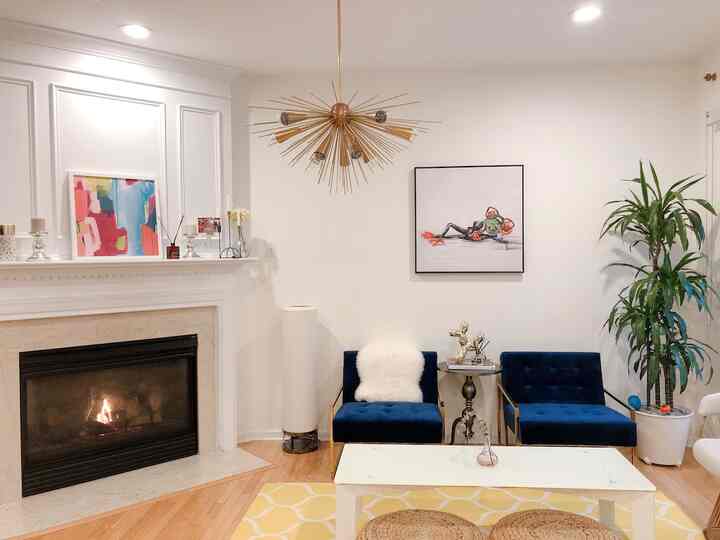 Modern and simple living room with white walls and ceiling, two dark blue armchairs centrally placed, and a gold chandelier