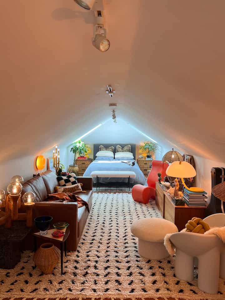Warm natural-toned loft bedroom featuring leather sofa, distinctive lighting, and cozy decor elements