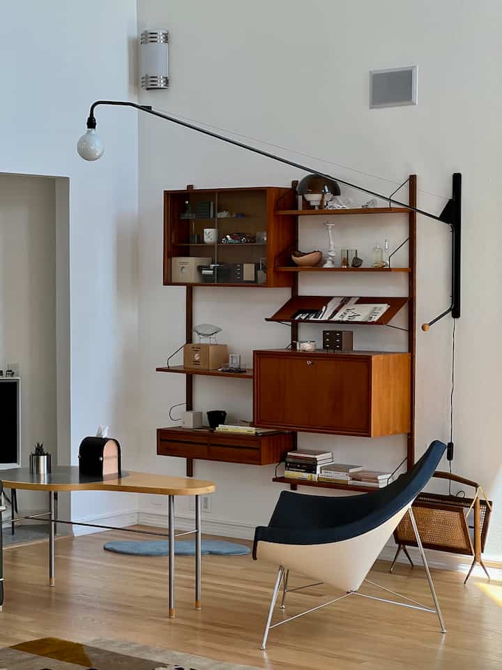 White walls and wood-tone floor in a mid-century modern living room featuring a Nelson Coconut armchair, wall shelves, and a pendant lamp creating a cozy atmosphere