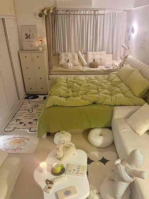 A beige and light green toned bedroom-living space featuring cushions and rugs creating a cozy atmosphere