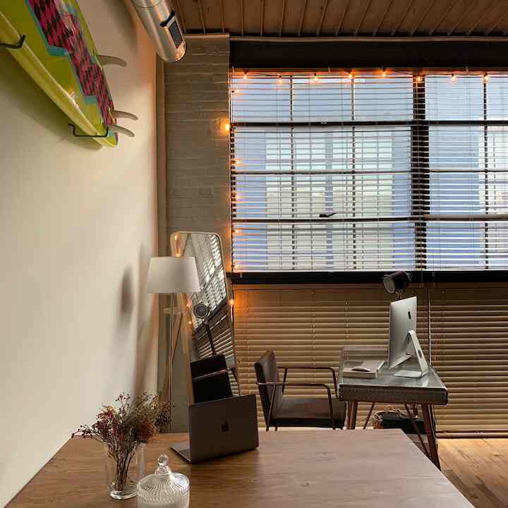 Natural tone home office with white walls and wood flooring, featuring an angled desk by the window and a full-length mirror enhancing spaciousness