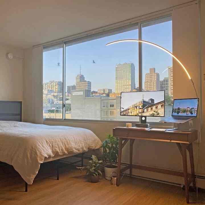A white and wood-toned single household bedroom featuring mid-century modern furniture and an arc floor lamp creating a cozy home office ambiance