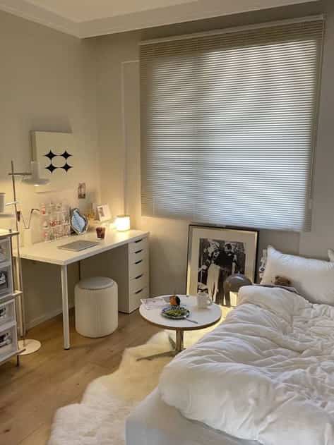 Bright ivory-toned studio bedroom featuring white bedding and modern desk with cozy, simple atmosphere