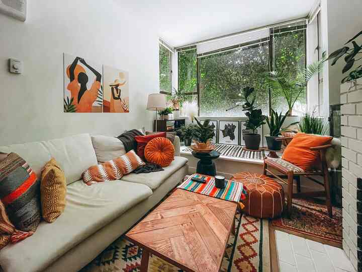 White and brown toned living room featuring bohemian style sofa, ottoman, and abundant plants creating a cozy atmosphere
