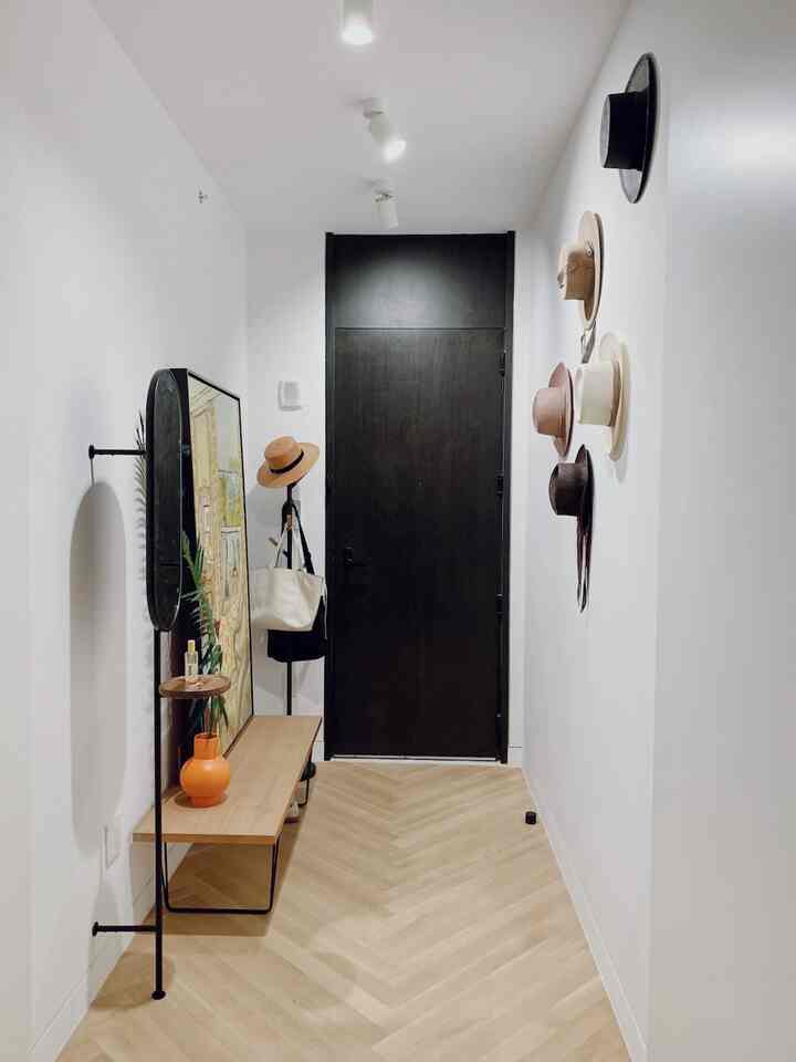 White and wood-tone narrow entrance featuring hanging hats on the wall and a sleek coat rack