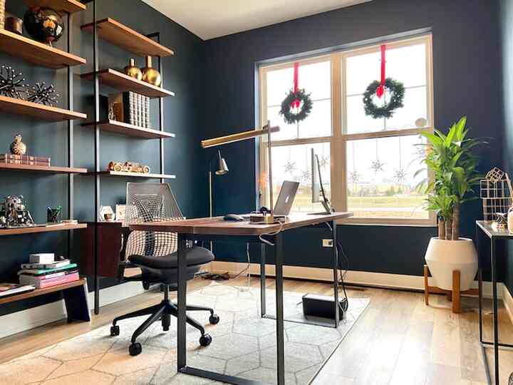 A sleek home office with dark blue walls, wood-tone desk, and black metal frame shelves creating a clean workspace