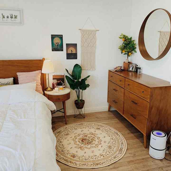 Bright white and brown toned bedroom featuring wooden bed, round rug, wood-framed mirror, and dresser providing cozy atmosphere